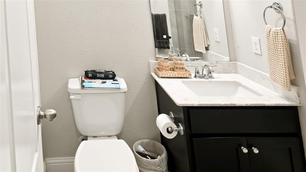 Black cabinetry, white composite countertop with integrated sink, dual-handle chrome faucet, wall-mounted mirror, and wall-mounted ring towel holder