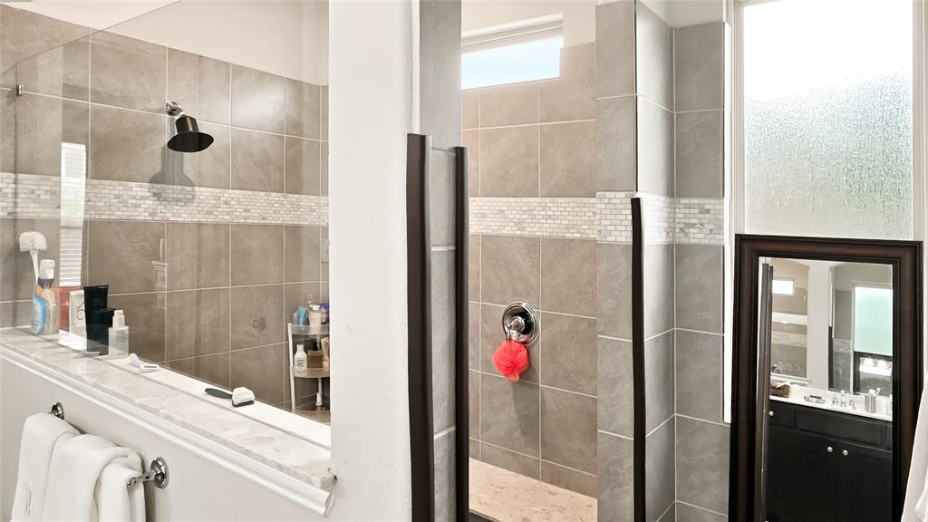 Walk-in shower featuring large-format stone-finish wall tiles, decorative mosaic tile accents, a glass enclosure, and an overhead rainfall showerhead
