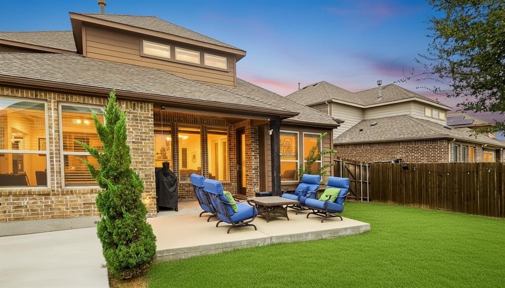Rear exterior featuring a brick facade, covered concrete patio, multiple window banks, and a privacy fence