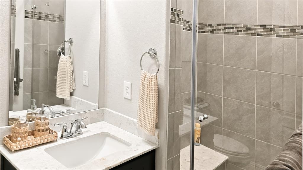 Bathroom featuring a vanity with a white composite countertop, an undermount rectangular sink, chrome hardware, a frameless glass shower enclosure with floor-to-ceiling tile, and a decorative tile accent inlay