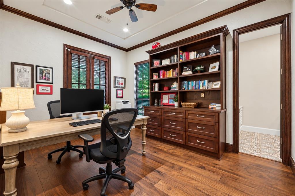 Hardwood flooring with a built-in wood-finish bookcase and storage, a tray ceiling, and a ceiling fan