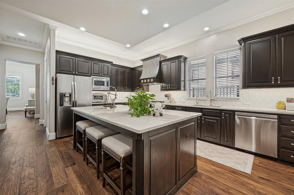 Kitchen featuring wood-finish flooring, dark wood cabinetry, stainless steel appliances, a center island with a light-toned countertop, and recessed lighting