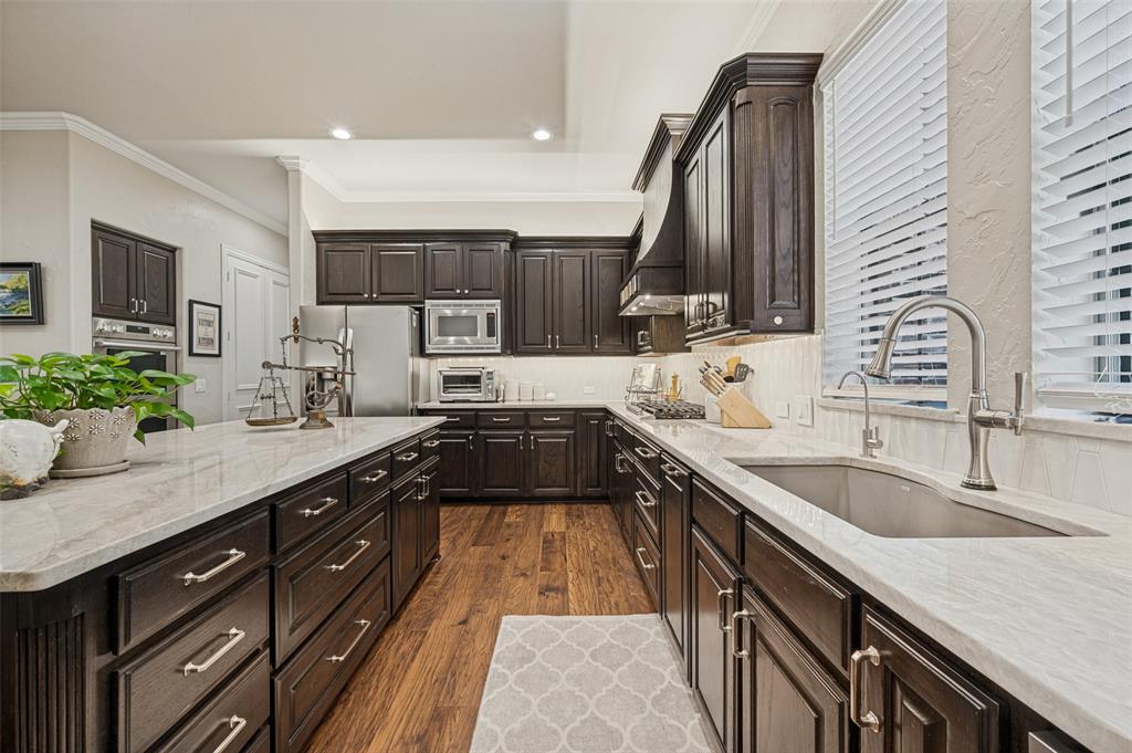 Gourmet kitchen featuring dark wood cabinetry with brushed metal hardware, white quartz countertops, stainless steel appliances, a professional-grade faucet with pull-down sprayer, and warm wood-finish flooring throughout the galley layout