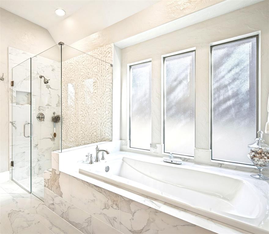 Built-in soaking tub, walk-in shower with glass enclosure, marble-style tile surround, decorative accent wall tile, and recessed lighting