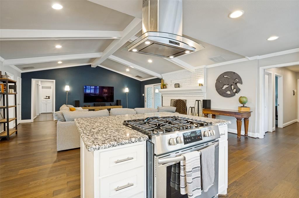 Kitchen island featuring a built-in stainless steel gas range with a matching range hood and granite countertop