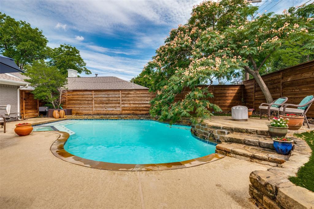 Inviting backyard featuring a free-form swimming pool with a stone coping border, a flagstone patio, and a stone retaining wall