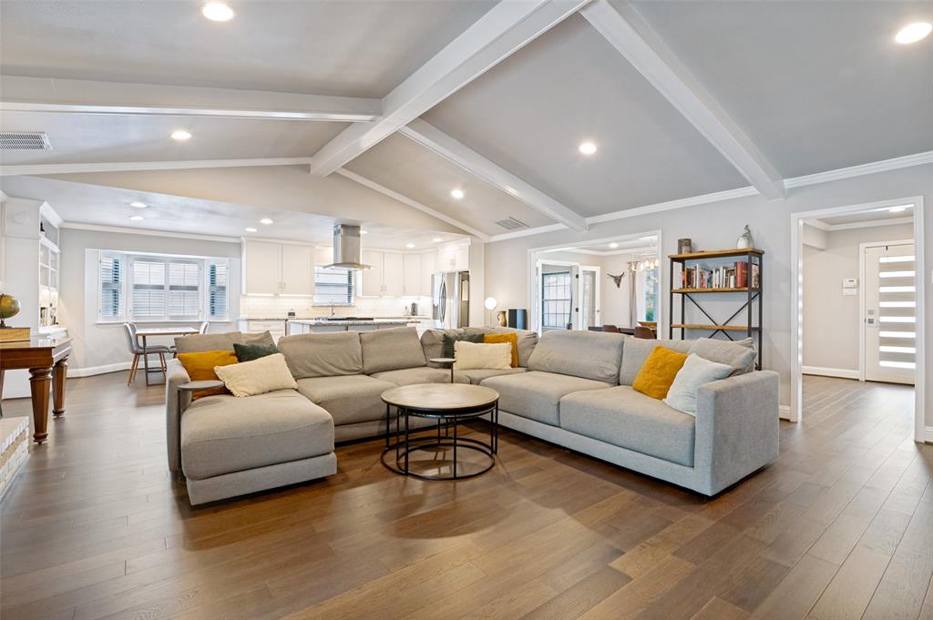 Spacious living area featuring wood-finish flooring, vaulted ceiling with exposed beams, and recessed lighting