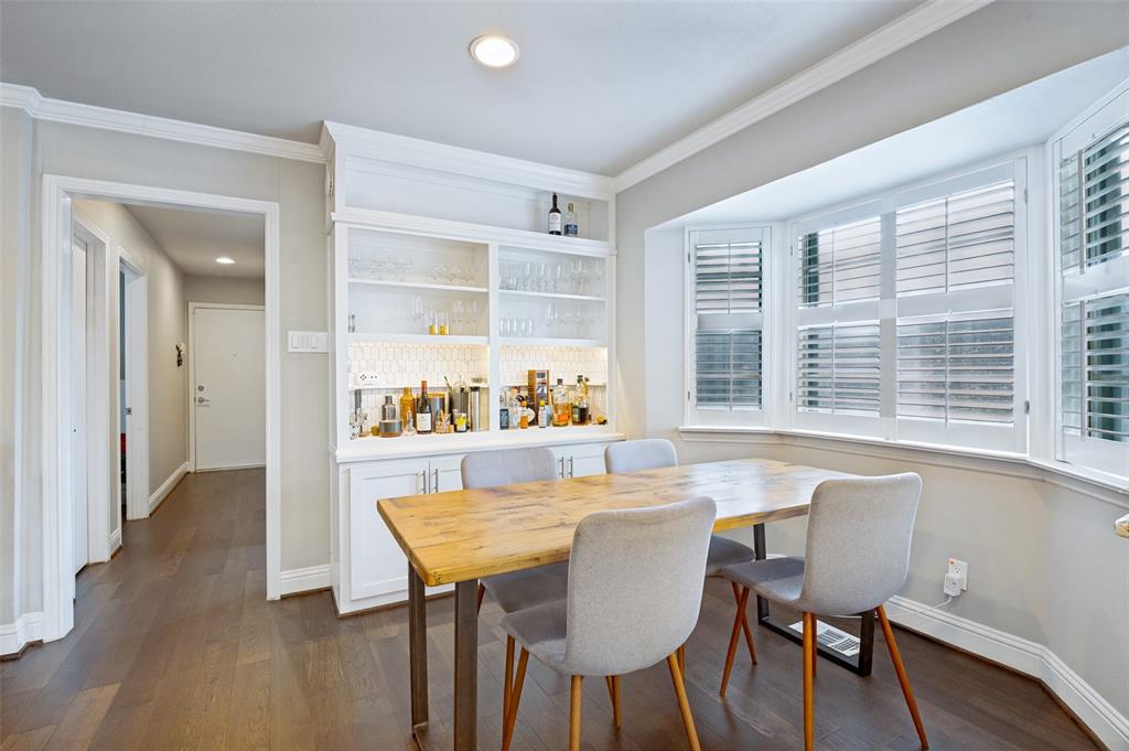 Built-in cabinetry with glass shelving and illuminated backsplash, wood-finish flooring, recessed lighting, crown molding, and a bay window featuring plantation shutters