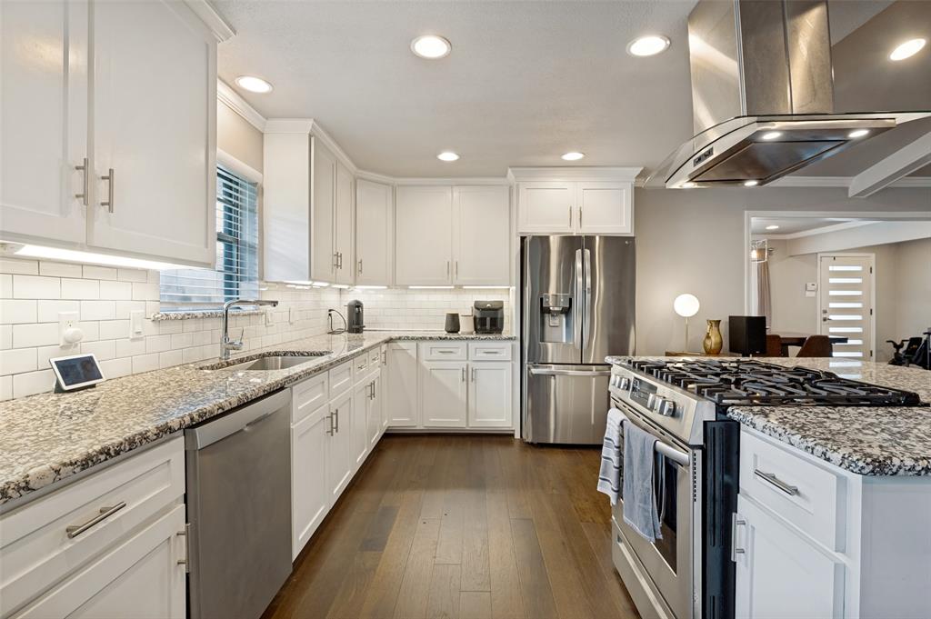 Kitchen featuring white shaker cabinetry, stainless steel appliances, speckled stone countertops, a subway tile backsplash, and wood-finish flooring