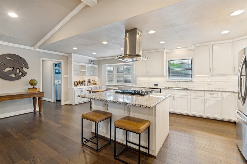 Kitchen featuring a central island with a gas cooktop and granite countertop, stainless steel range hood, white shaker-style cabinetry, subway tile backsplash, and wood-finish flooring