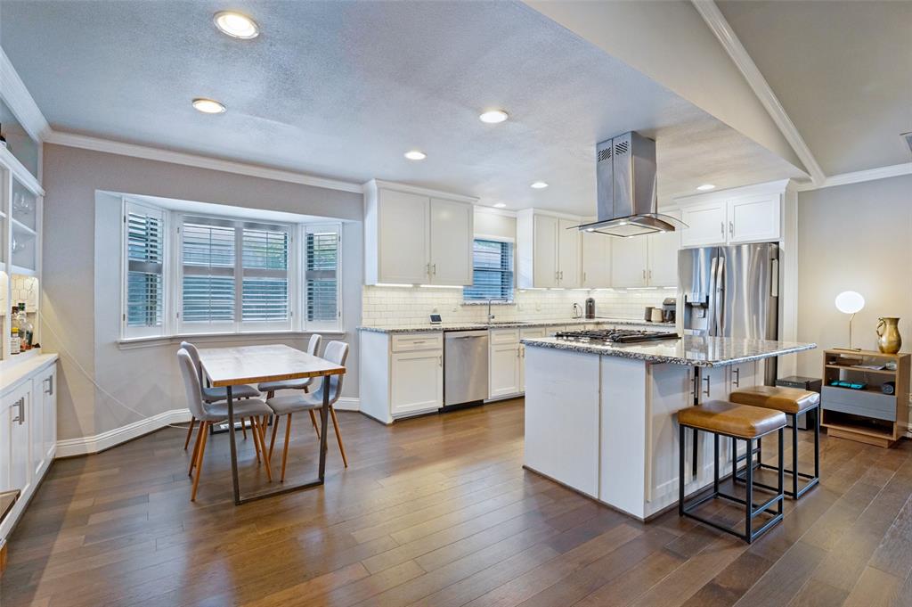 Kitchen featuring wood-finish flooring, white cabinetry, a built-in kitchen island with seating, a stainless steel range hood, and recessed lighting