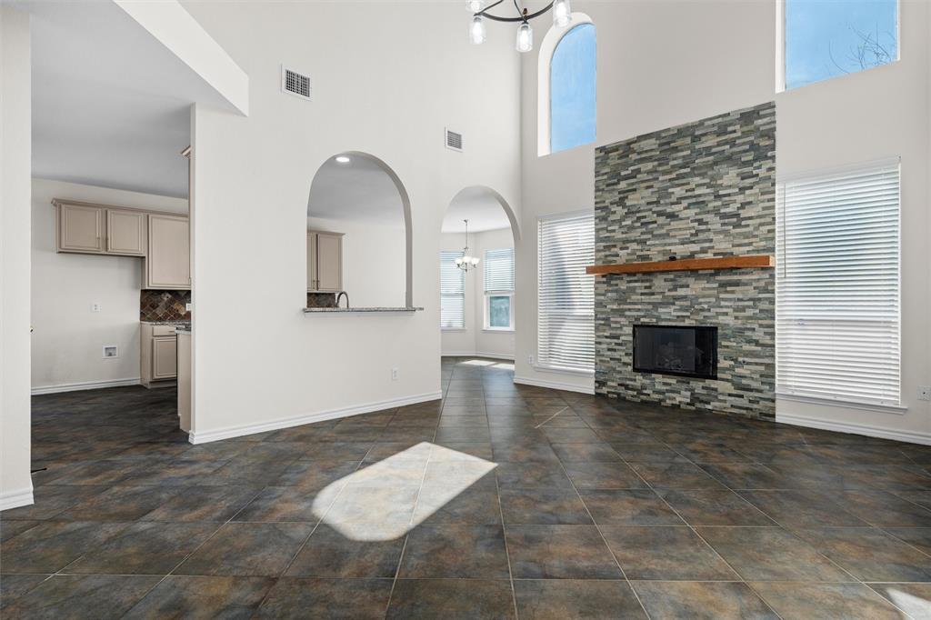 Vaulted ceilings with an arched window, a stone-clad fireplace with a wood mantel, tiled flooring, and arched doorways