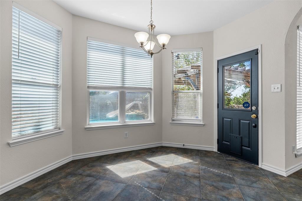 Bay window with multiple windows, overhead chandelier, and a paneled door with glass insert, all above dark-toned tile flooring