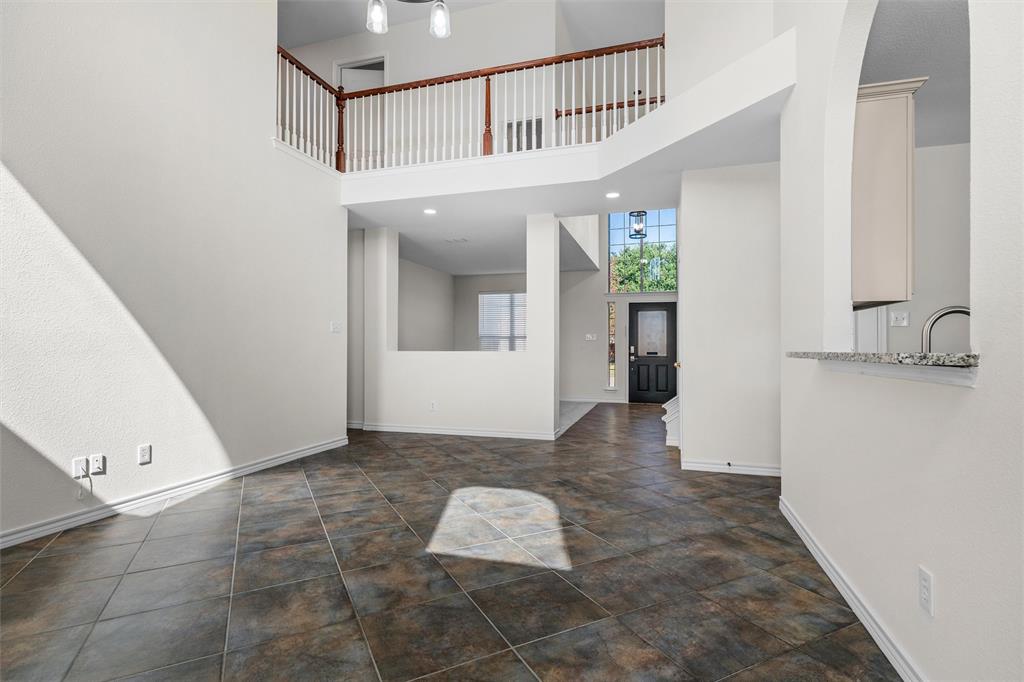 Two-story living space featuring high ceilings, tile flooring, and an open upper-level landing with wood and white balusters