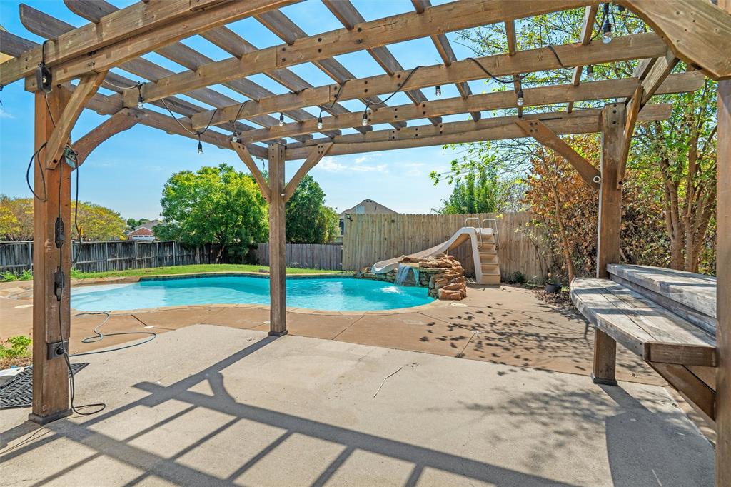 Expansive concrete patio with a wooden pergola, private swimming pool, and rock waterfall feature