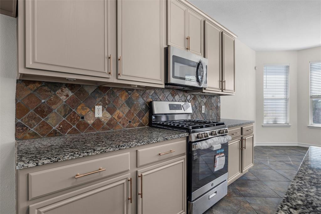 Kitchen featuring granite-style countertops, under-cabinet lighting, stainless steel appliances, a gas range, and a tiled backsplash