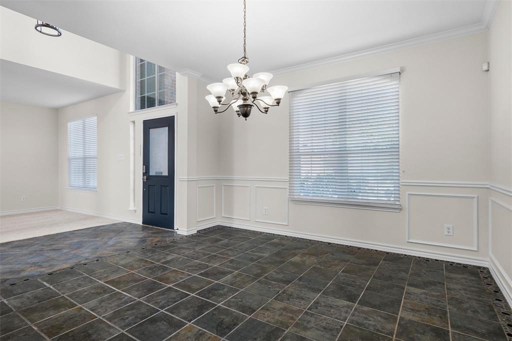 Tile flooring, decorative wall paneling, window with blinds, front door with glass insert, and a chandelier