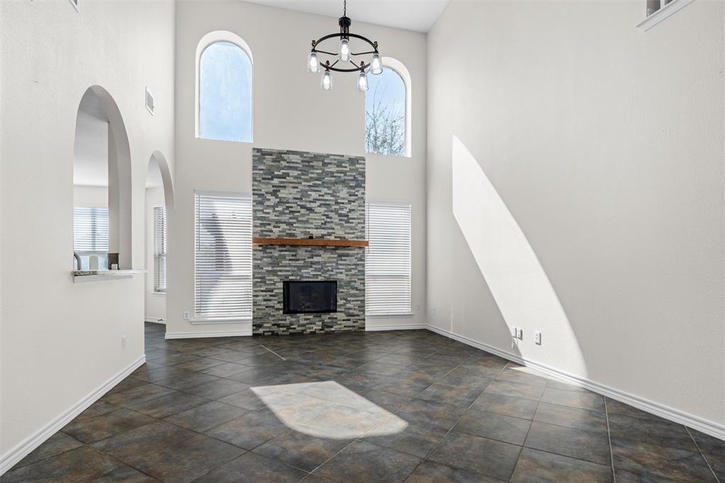 Vaulted ceiling with a contemporary chandelier, arched windows, tile flooring, and a fireplace with a stone surround and wood mantle
