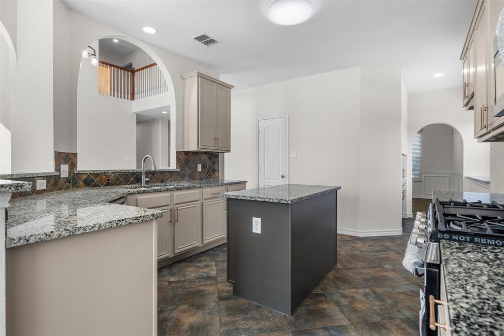 Kitchen featuring a central island, granite countertops, tile backsplash, stainless steel gas range, and recessed lighting