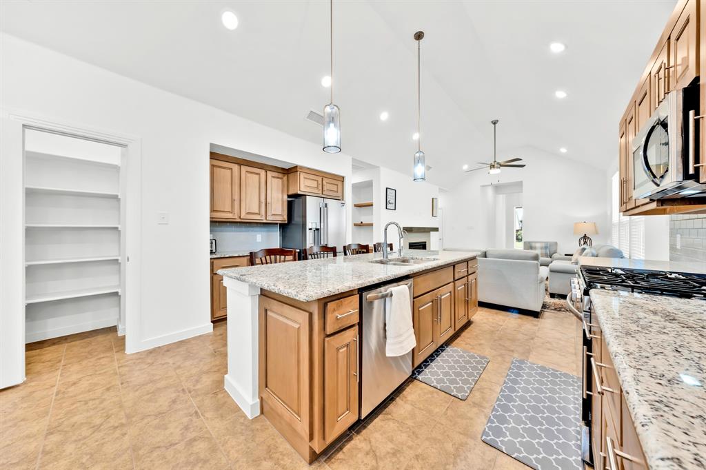 Kitchen featuring a large central island with a sink, granite countertops, stainless steel appliances, and wood cabinetry