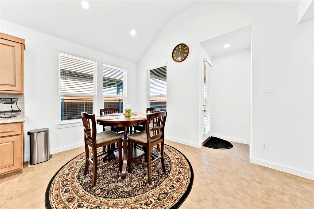 Vaulted ceiling, recessed lighting, multiple windows with blinds, wood-finish cabinetry, and light-toned tile flooring
