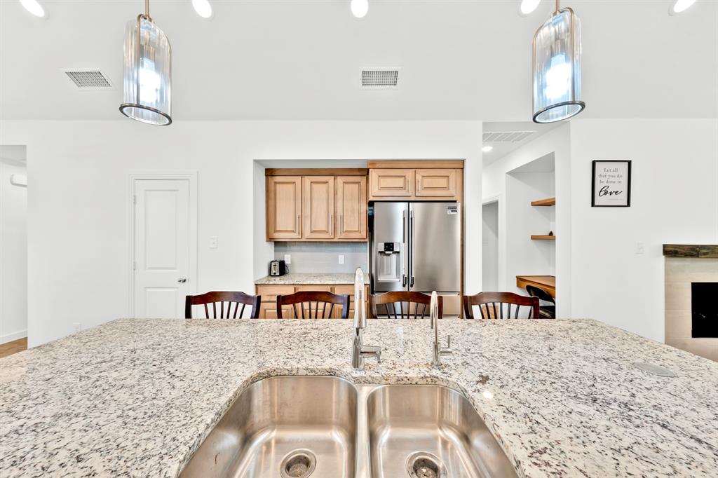 Kitchen island with a double stainless steel sink and granite countertop, stainless steel refrigerator, and wood cabinetry