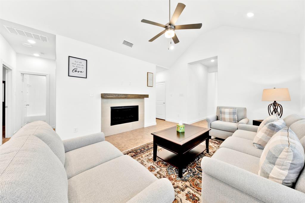Vaulted ceiling with an integrated ceiling fan, fireplace with a wood mantel, tile flooring, recessed lighting, and a white interior