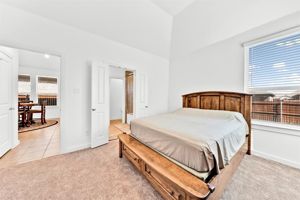 Vaulted ceiling, neutral carpet flooring, and a large window with blinds