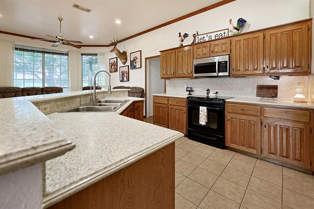 Kitchen featuring wood cabinetry, solid-surface countertops, tile flooring, built-in microwave, and a double-basin stainless steel sink with a high-arch faucet