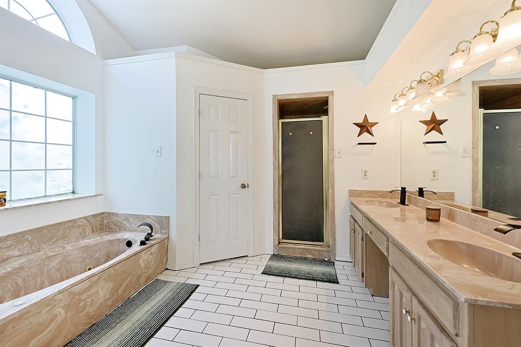 Bathroom featuring a dual-sink vanity with stone-finish countertops, a soaking tub with matching surround, a glass-enclosed shower, and white tile flooring