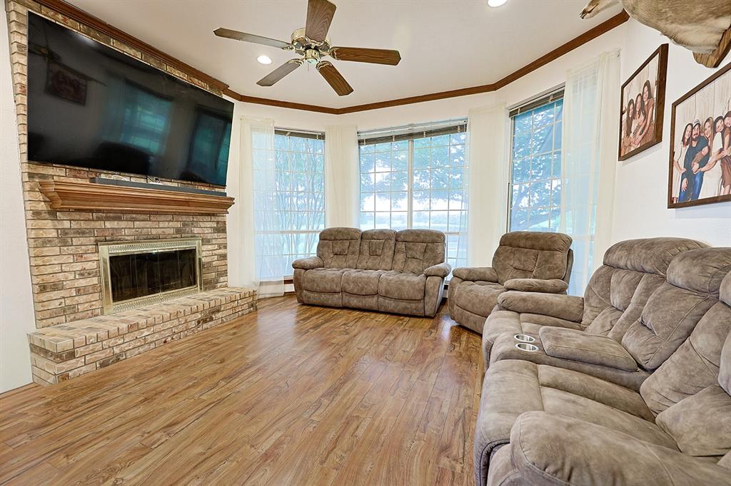 Brick fireplace surround with a wood mantel, wood-finish flooring, bay window configuration, and a ceiling fan with integrated lighting