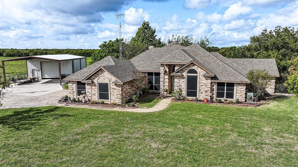 Single-story masonry exterior featuring a multi-gabled roofline, concrete driveway, attached metal-framed workshop, and landscaping beds