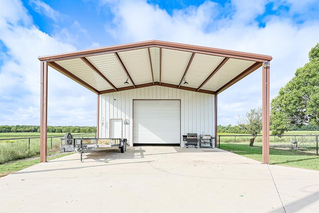 Metal-sided detached structure featuring a high-clearance carport, concrete foundation, roll-up overhead door, and integrated lighting
