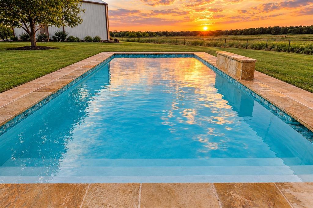 In-ground rectangular swimming pool featuring stone-finish coping, a built-in water feature, integrated stairs, and expansive lawn area