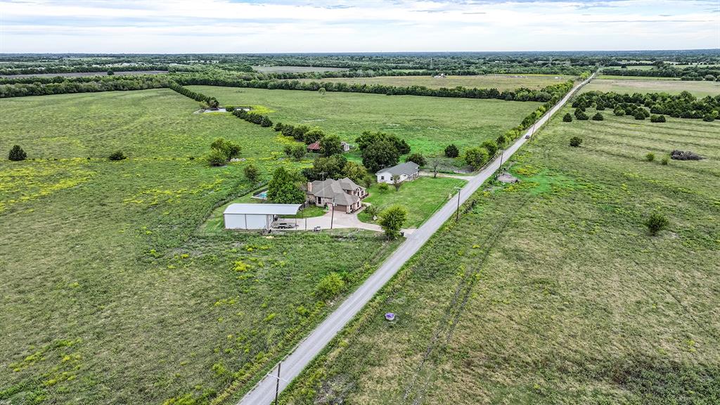 Aerial perspective of a multi-structure property featuring expansive acreage, a residential dwelling, a detached metal-sided workshop, and a paved driveway