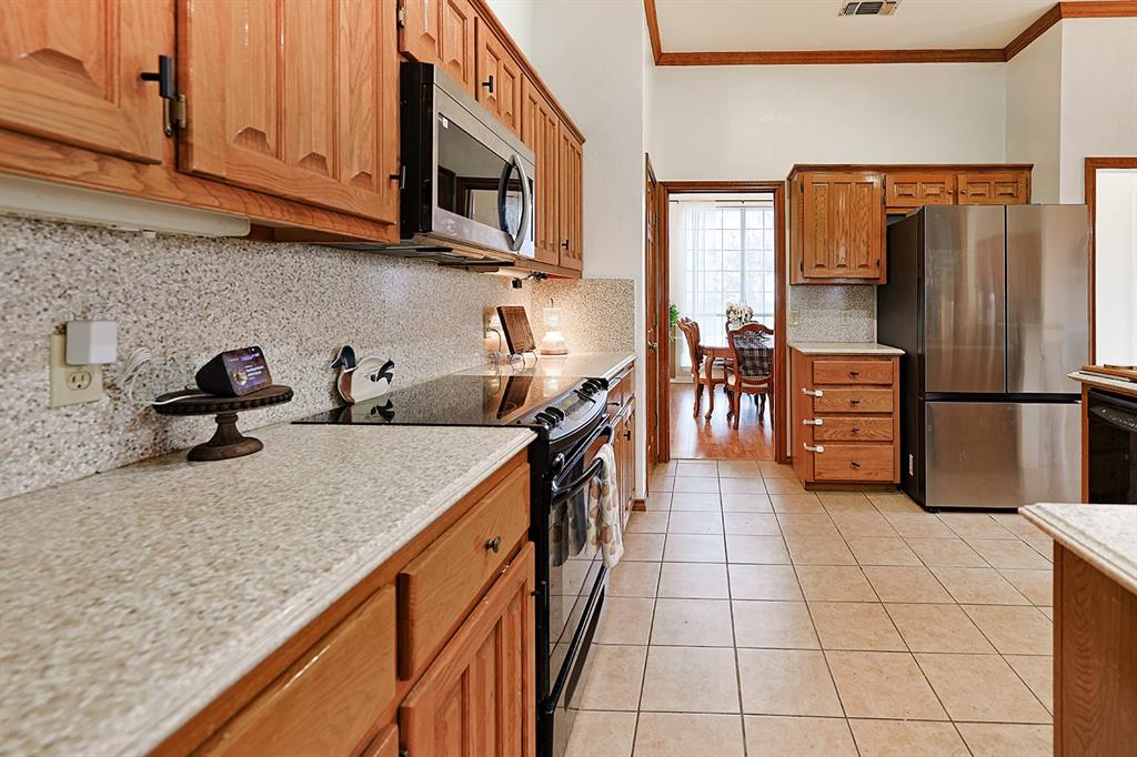 Kitchen featuring stained wood cabinetry, stone-finish countertops, stainless steel appliances, and ceramic tile flooring