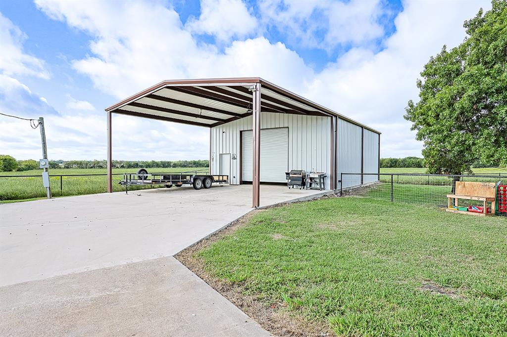 Metal-sided workshop building with a concrete parking pad, oversized roll-up door, side entry door, and extended metal-roofed carport structure