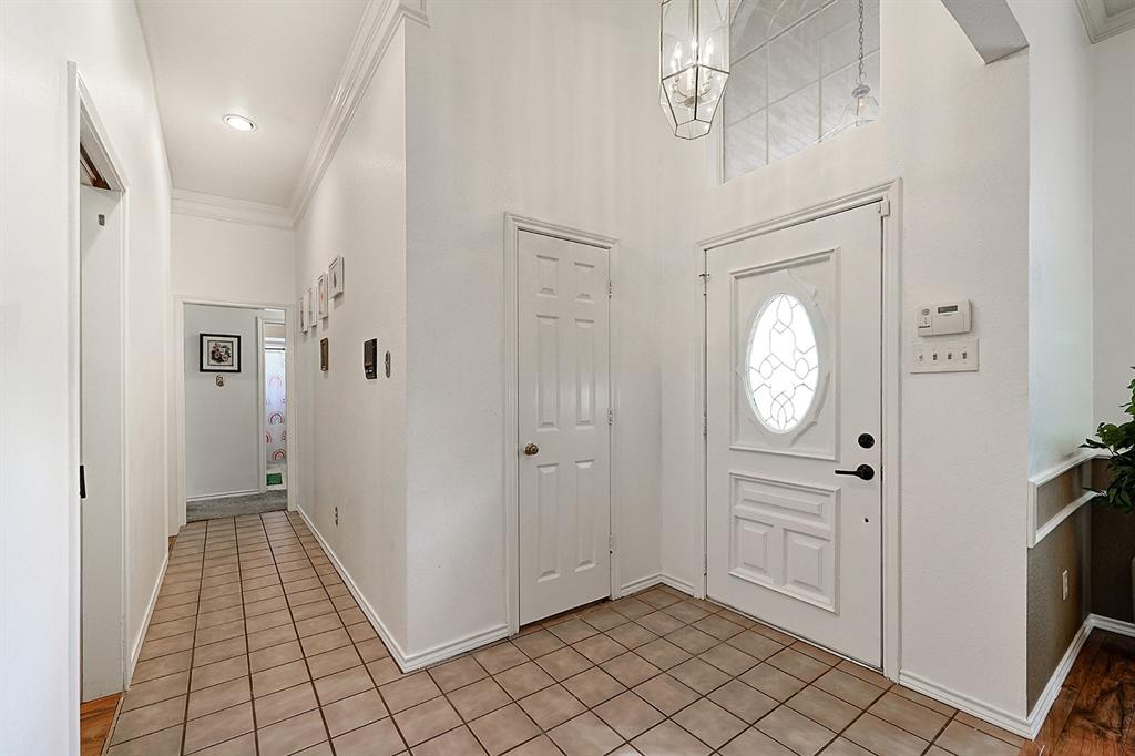 Foyer featuring high ceilings, a transom window above an oval-glass entry door, ceramic tile flooring, and a multi-light geometric pendant fixture
