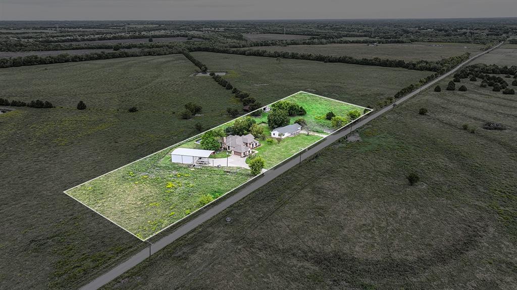 Aerial perspective of property featuring two residences, a metal-roofed detached structure, paved driveway, and expansive acreage
