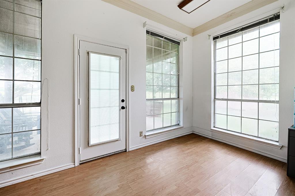 Sun-filled room featuring wood-finish flooring, grid-patterned windows, crown molding, and a glass-paneled exterior door