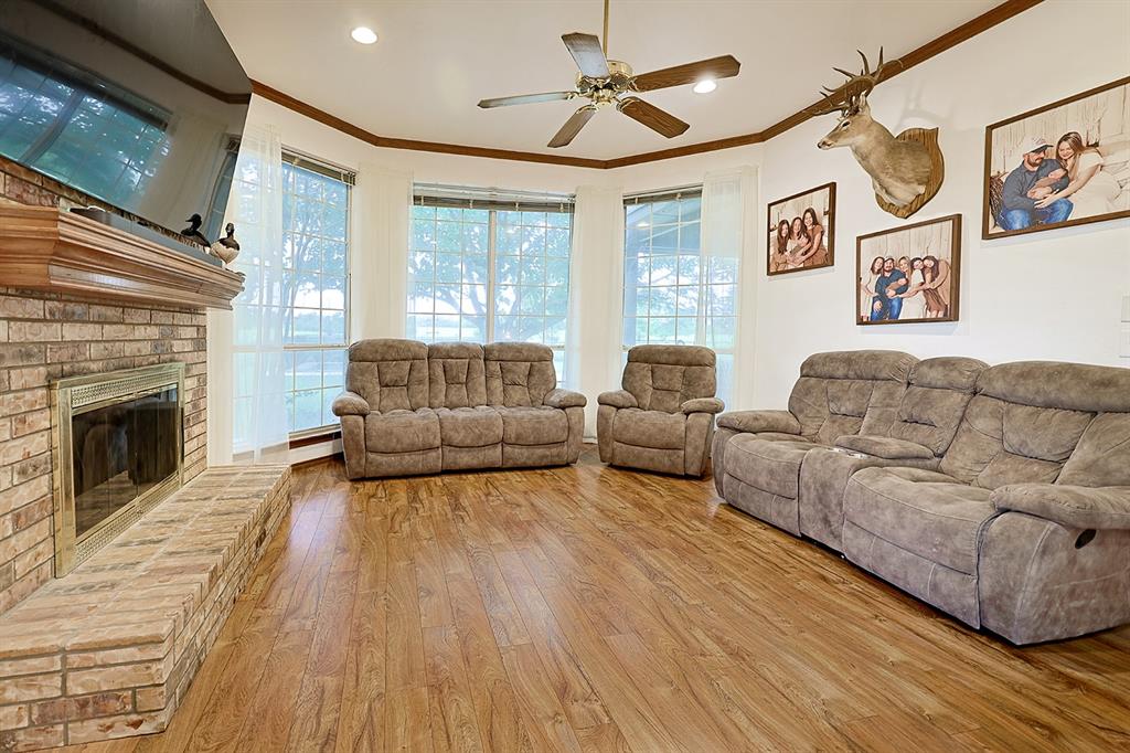 Brick fireplace featuring a raised hearth and wooden mantel, wood-finish flooring, tray ceiling with a center fan, and multiple large windows
