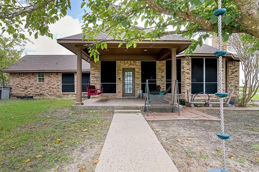 Brick exterior featuring a covered patio with column supports, a concrete walkway, and a glass-paneled entry door