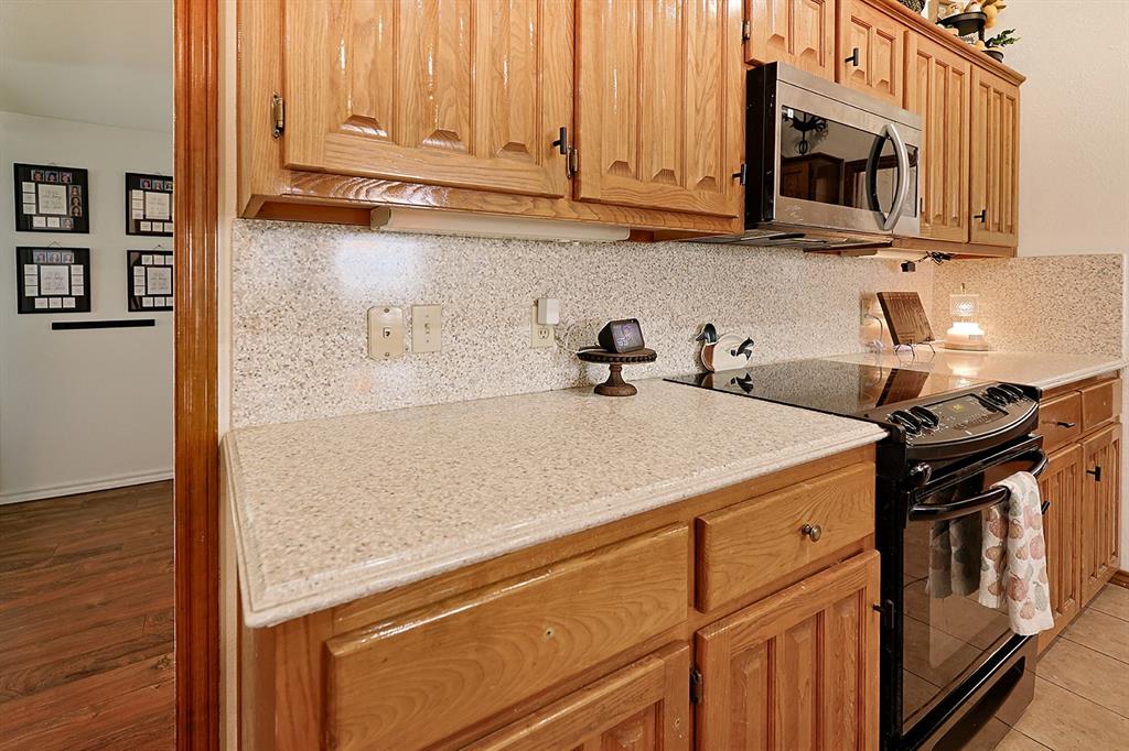 Kitchen featuring raised-panel wood cabinetry, speckled composite countertops, a full-height matching backsplash, a built-in stainless steel microwave, and a black glass-top range