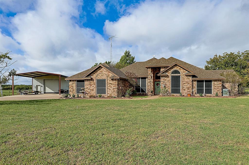 Brick exterior residence featuring arched windows, a multi-gabled roofline, an expansive lawn, and a detached metal-frame workshop with a covered carport