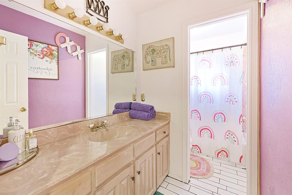Bathroom vanity with a stone-finish countertop, integrated basin, wood-cabinetry storage, full-width wall mirror, and overhead vanity lighting