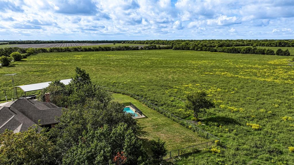 Expansive acreage featuring a fenced swimming pool, metal-roofed carport, mature trees, and open meadowland