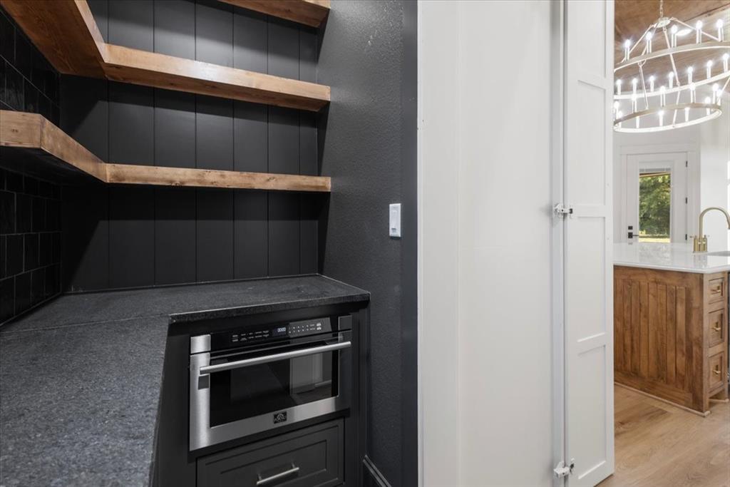 Built-in stainless steel microwave, dark countertop, open wood-finish shelving, and white paneled doors
