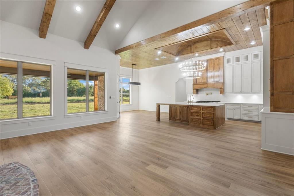 Vaulted ceiling with exposed wood beams, wood-finish flooring, recessed lighting, kitchen island with wood cabinetry, and white kitchen cabinetry