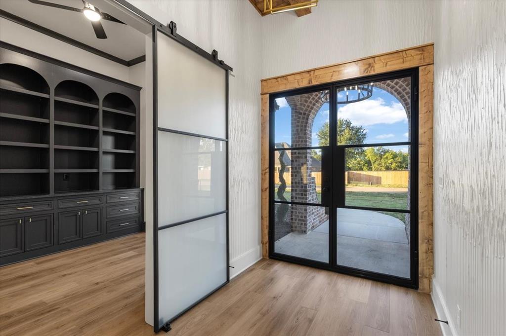Wood-finish flooring, built-in cabinetry, frosted glass barn door, and a black-framed glass door with timber trim