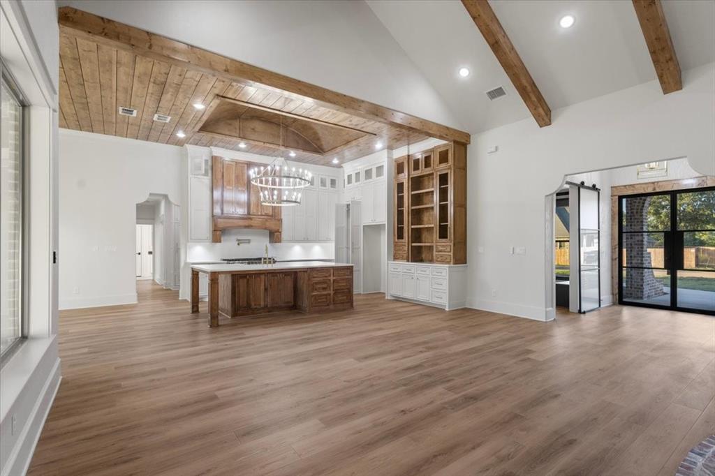 Vaulted ceiling with exposed wood beams, wood-finish flooring, built-in cabinetry with shelving, recessed lighting, and a kitchen island with built-in storage